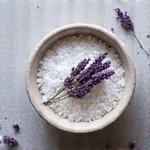 Garam laut kristal dan kuntuman bunga lavender kering dalam mangkuk, mencerminkan ketenangan. (Organik)